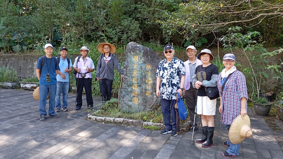 8人站在石碑前合影，背景為綠樹林蔭，氣氛輕鬆愉快。圖片