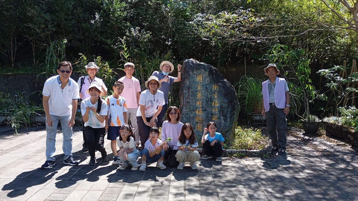 成人與孩童在石碑前合影，陽光明亮，氣氛愉快自然。圖片