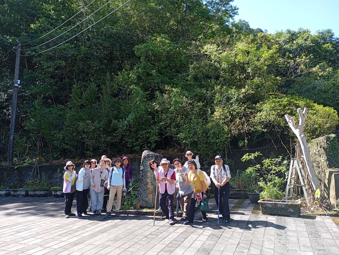 莊社大青草班成員在晴朗的天氣下，於衛生福利部『國家藥用植物園』石碑前開心合影。圖片